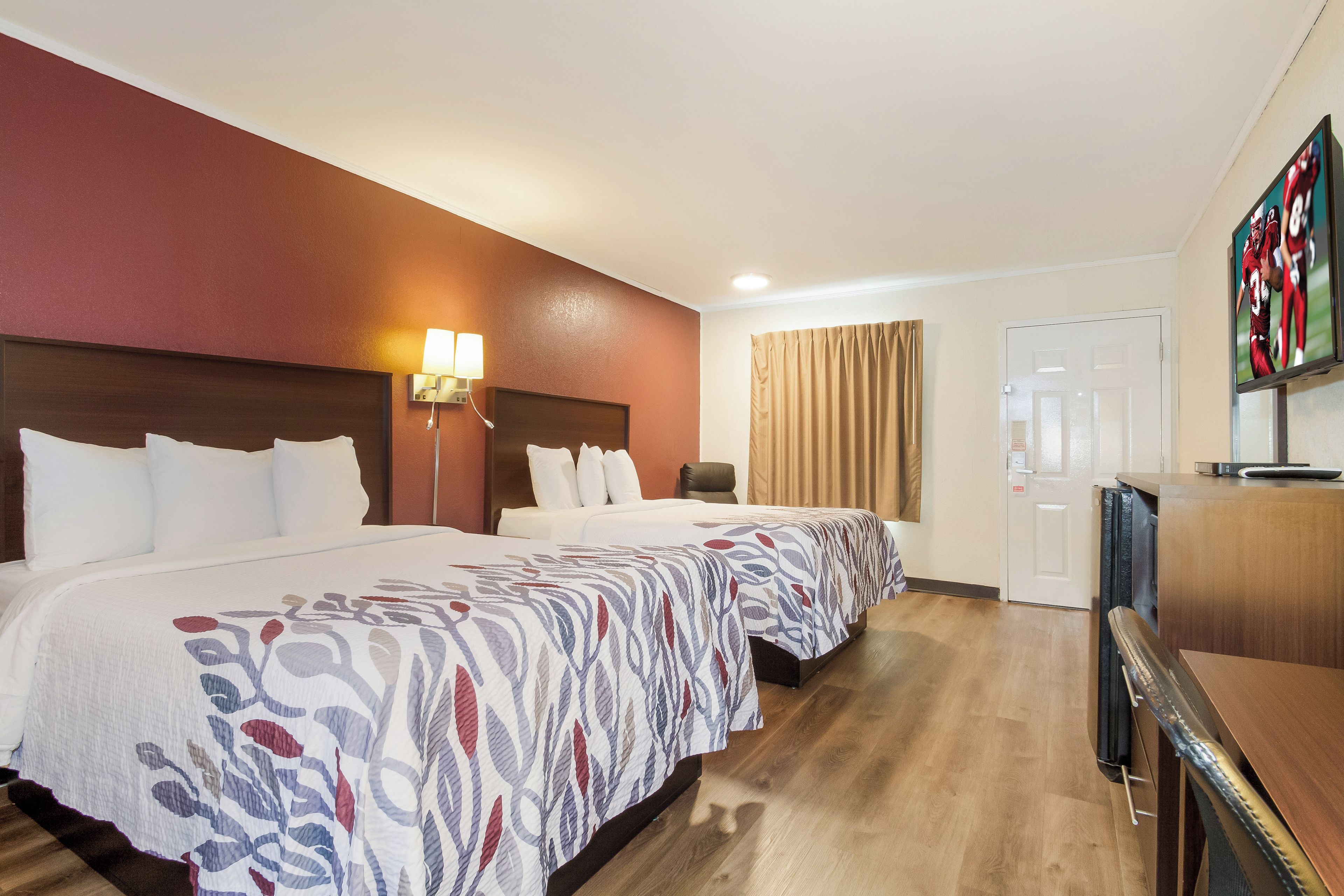 A hotel room with a large bed, a desk, a television, and a door.