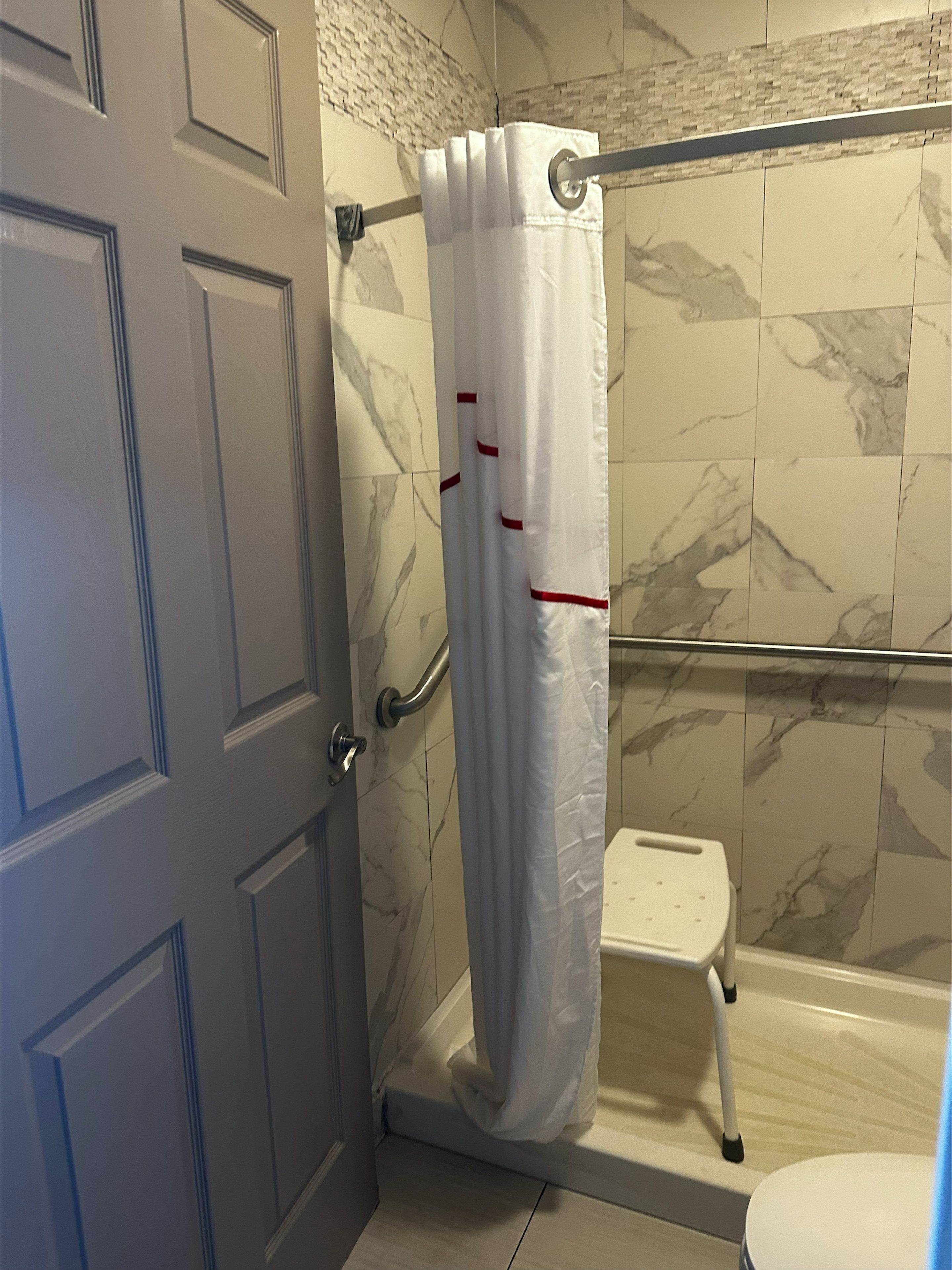 Un baño con cortina de ducha, barra de apoyo y un pequeño escalón que lleva al inodoro.