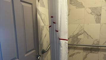 Un baño con cortina de ducha, barra de apoyo y un pequeño escalón que lleva al inodoro.