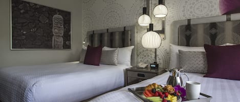 Camera d'albergo con due letti, un comodino con una lampada, un vassoio con frutta e una caffettiera.