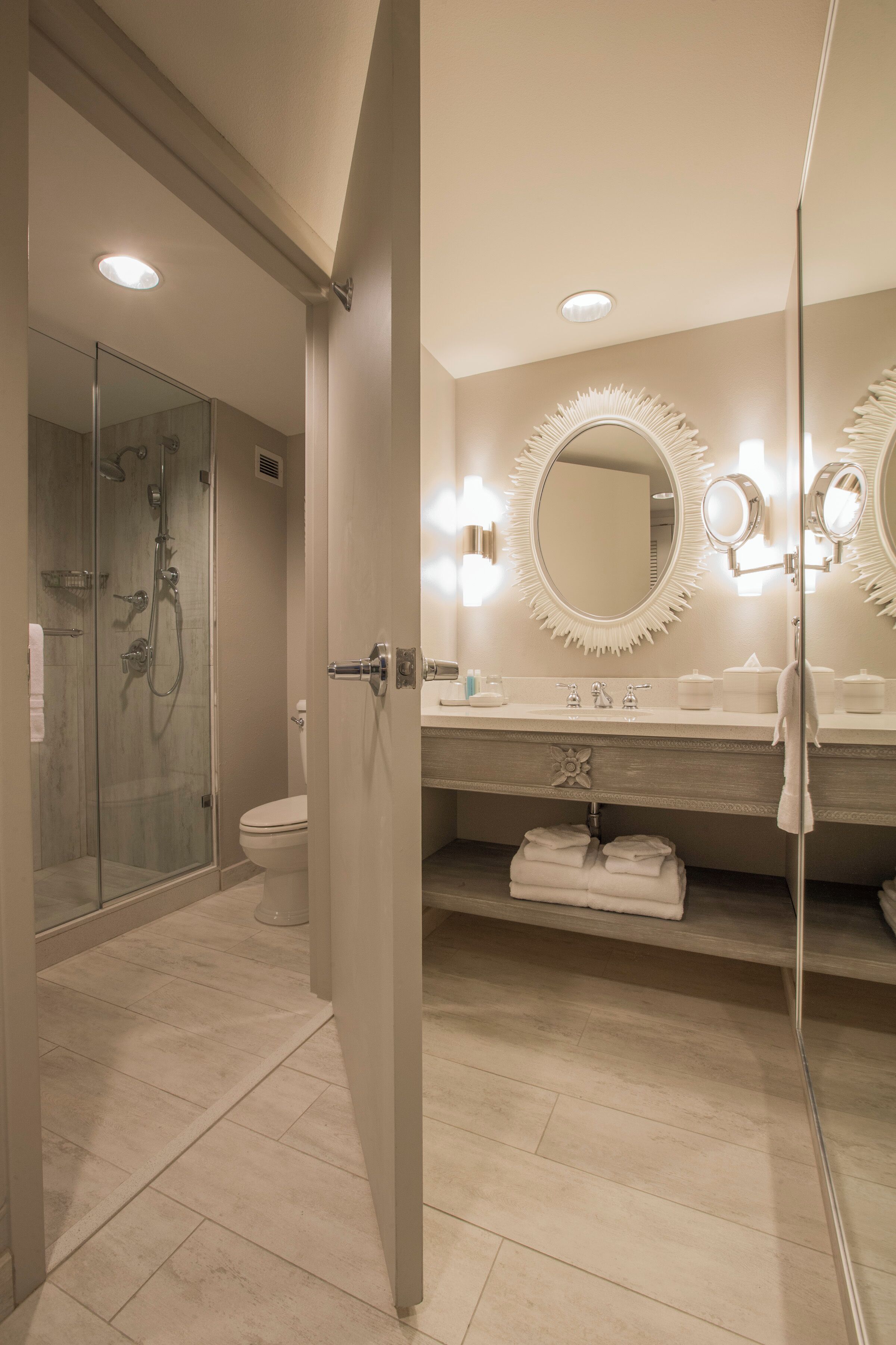 Een moderne badkamer met een douchecabine van glas, een toilet en een wastafel met een grote spiegel en wandlampen.