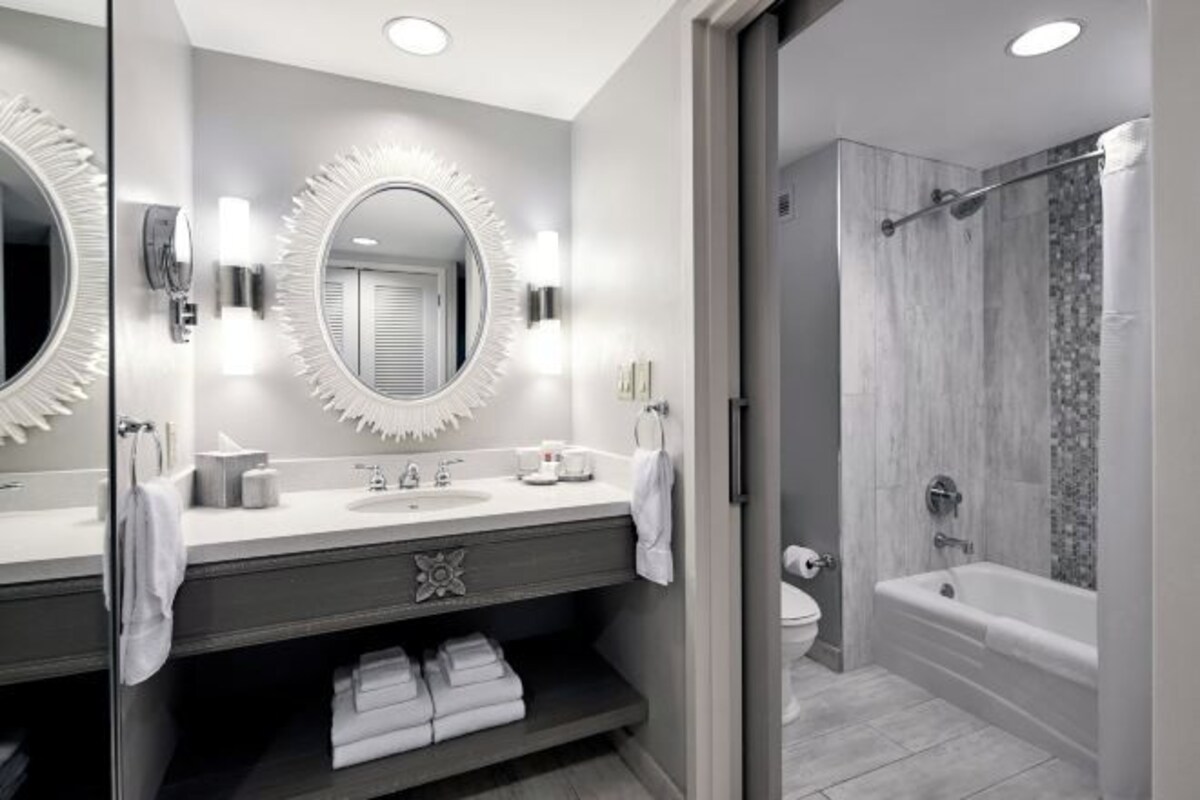A modern bathroom with a large mirror, two sinks, a vanity, and a shower area.