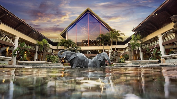 A hotel with a large reflective pool, two elephant statues, and a modern building with a glass facade. - Universal’s Loews Royal Pacific Resort (Orlando)