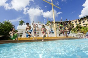 Une piscine où des gens sautent dans l’eau, un toboggan aquatique et un bâtiment sur lequel on peut lire l’inscription « ROYAL BAHAMAS ».