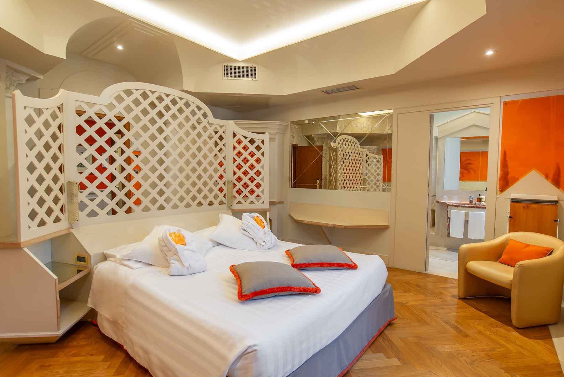 A modern hotel room with a large bed, a seating area, and a bathroom visible through a glass partition.