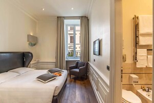 A hotel room with a large bed, a chair, a TV, and a bathroom with a sink and toilet.