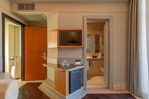 A hotel room with a wooden door, a small kitchenette with a TV, a mini-fridge, and a glass-top table.