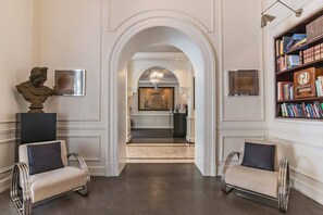 A hallway with two armchairs, a bust sculpture, a large painting, and a bookshelf.