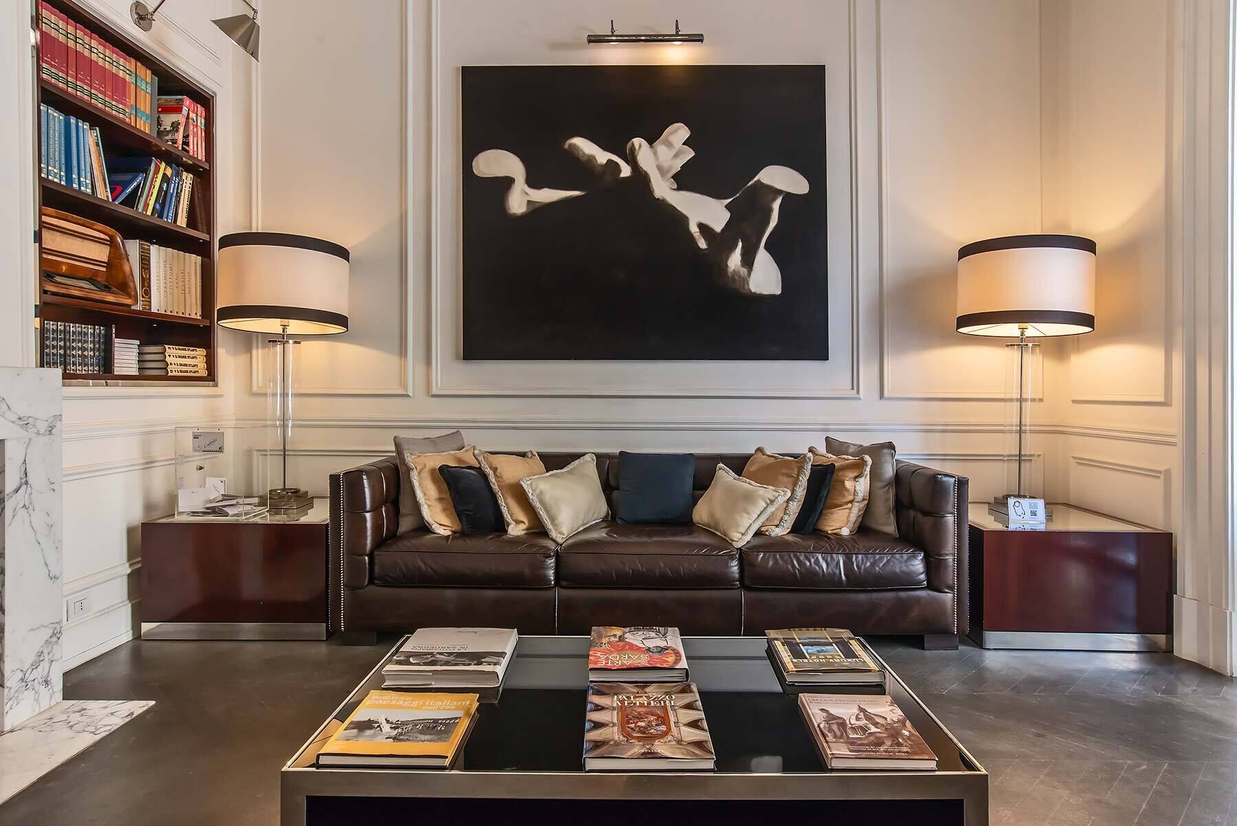 A modern living room with a leather sofa, a coffee table with books, a bookshelf, and two floor lamps.