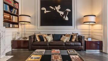 A modern living room with a leather sofa, a coffee table with books, a bookshelf, and two floor lamps.