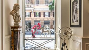 Un vestíbulo con una estatua de mármol, una puerta de cristal que da al exterior, una escultura de metal y un cuadro en la pared.