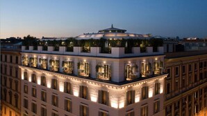 Un hotel de varios pisos con jardín en la azotea, ventanas iluminadas y un estilo arquitectónico clásico.