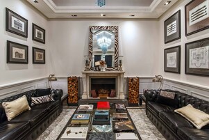 Ein geräumiges Wohnzimmer mit Kamin, Ledersofas, einem Couchtisch mit Büchern und gerahmten Bildern an den Wänden.