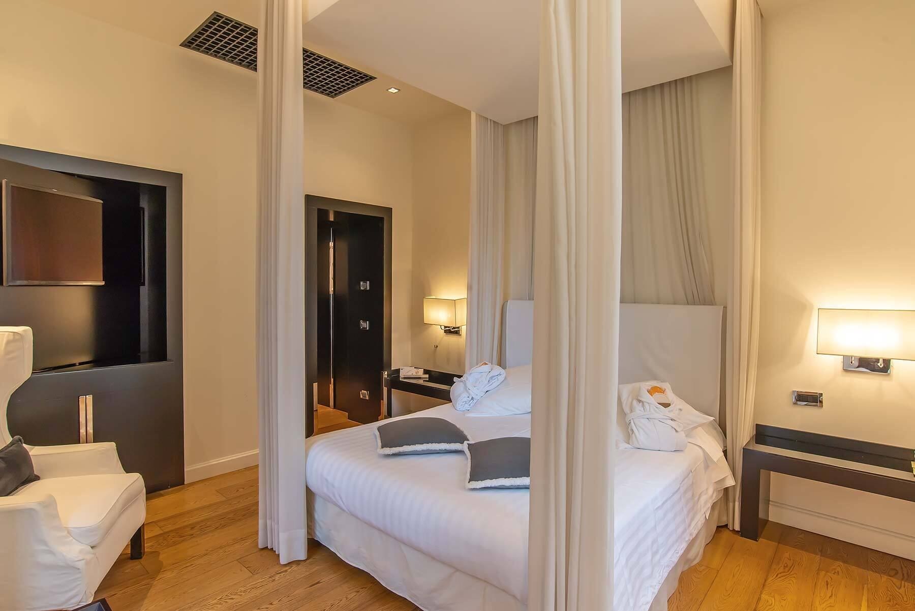 A hotel room with a bed, a nightstand, a lamp, a mirror, and a door.
