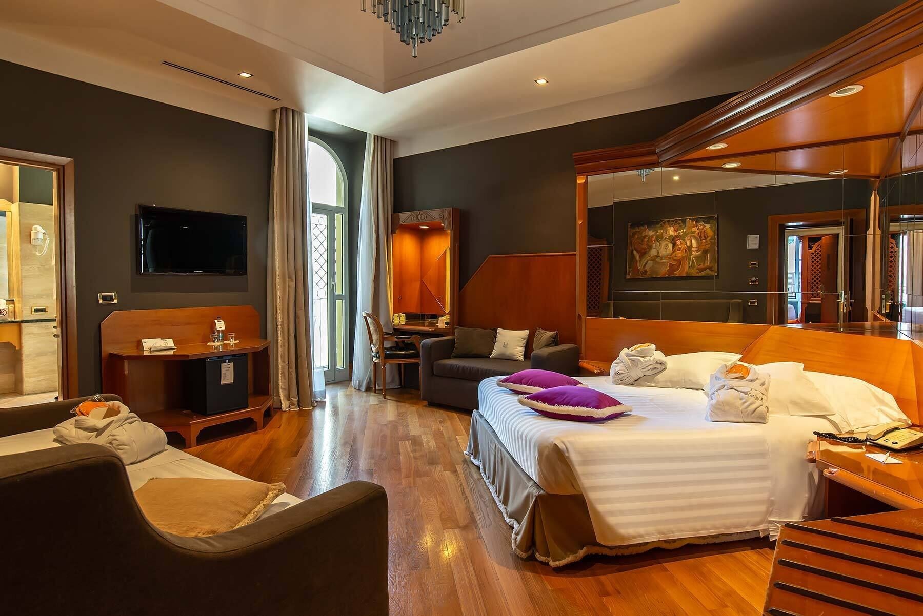 A modern hotel room with a large bed, a desk, a chair, a TV, and a bathroom visible through an open door.