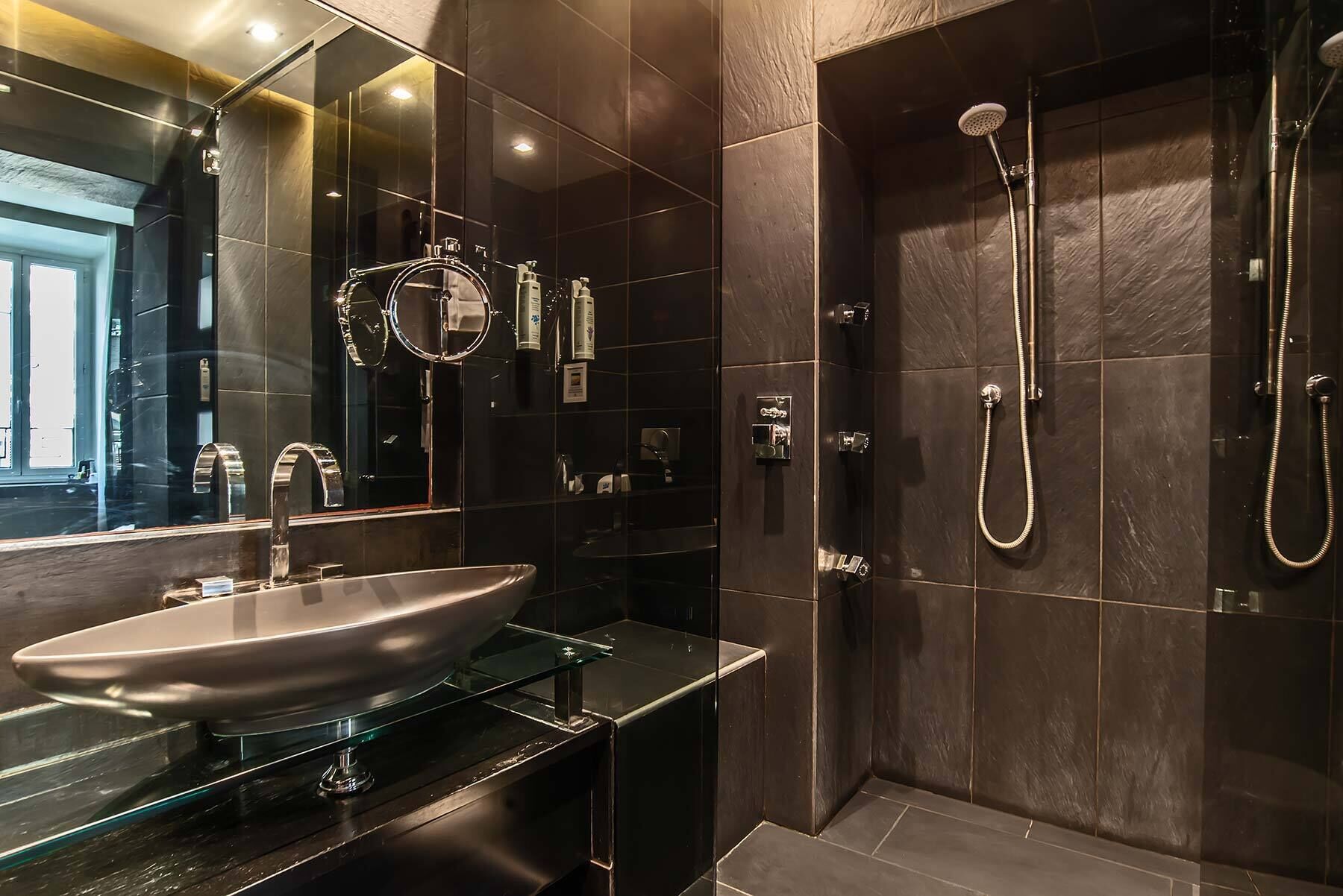 Une salle de bain moderne dotée d’un lavabo entouré de parois en verre, d’un grand miroir et d’une douche à l’italienne avec un pommeau de douche amovible.