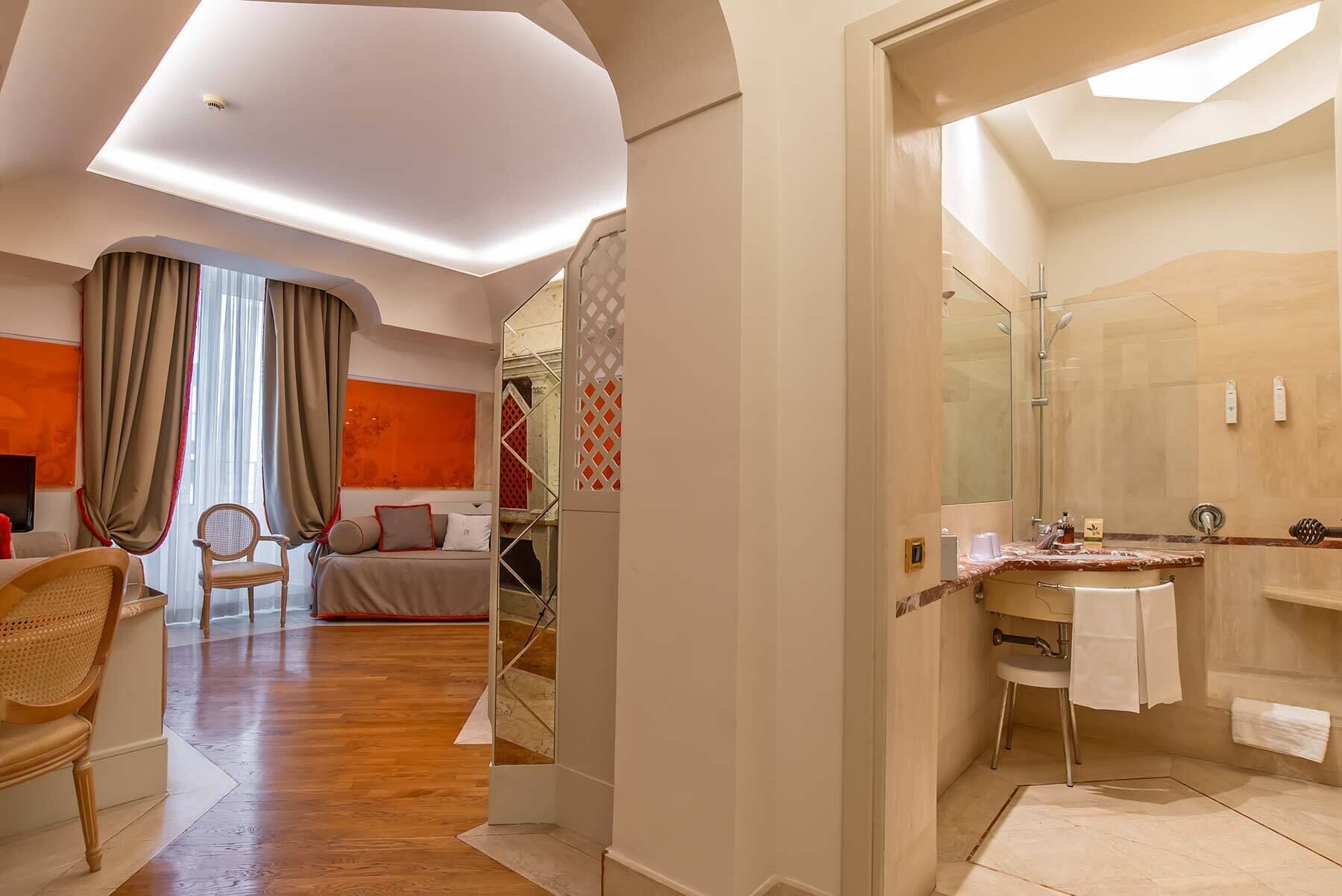 A hotel room with a bed, a chair, a bathroom with a shower, and a large window with curtains.