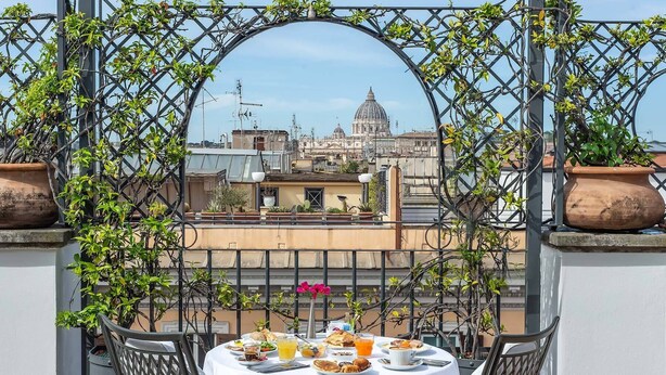 Mesa de balcón con alimentos para desayuno, con vista a un paisaje urbano que incluye una cúpula imponente.
