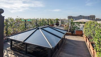 Una terraza en la azotea con techo de vidrio, cubierta de madera, plantas en macetas y vistas de la ciudad.