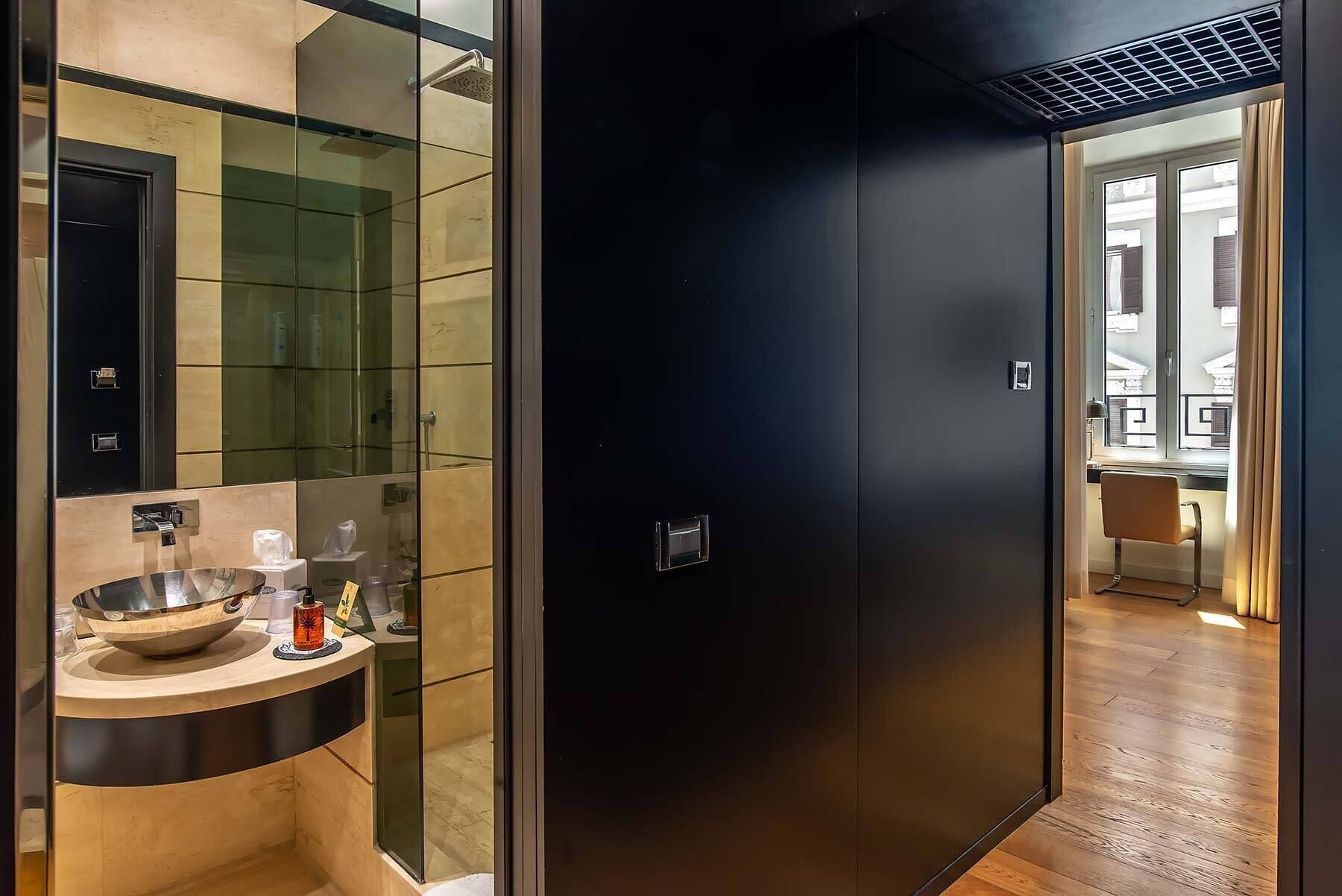 A modern bathroom with a glass shower enclosure, a sink with a bowl, and a dark door leading to a kitchen area.