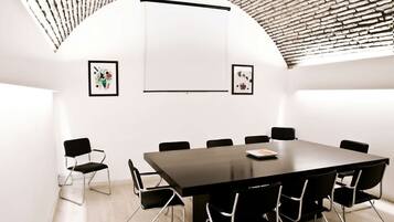 A conference room with a large black table, black chairs, a projector screen, and two framed pictures on the walls.