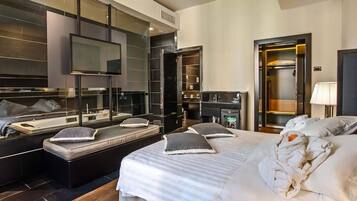 A modern hotel room with a large bed, a seating area with a bench, a vanity with a mirror, and a walk-in closet.