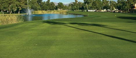 Un parcours de golf avec un étang, des arbres et un ciel dégagé.
