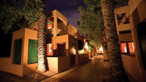 Vista nocturna d'un passadís d'hotel amb diversos pisos, palmeres i il·luminació càlida.