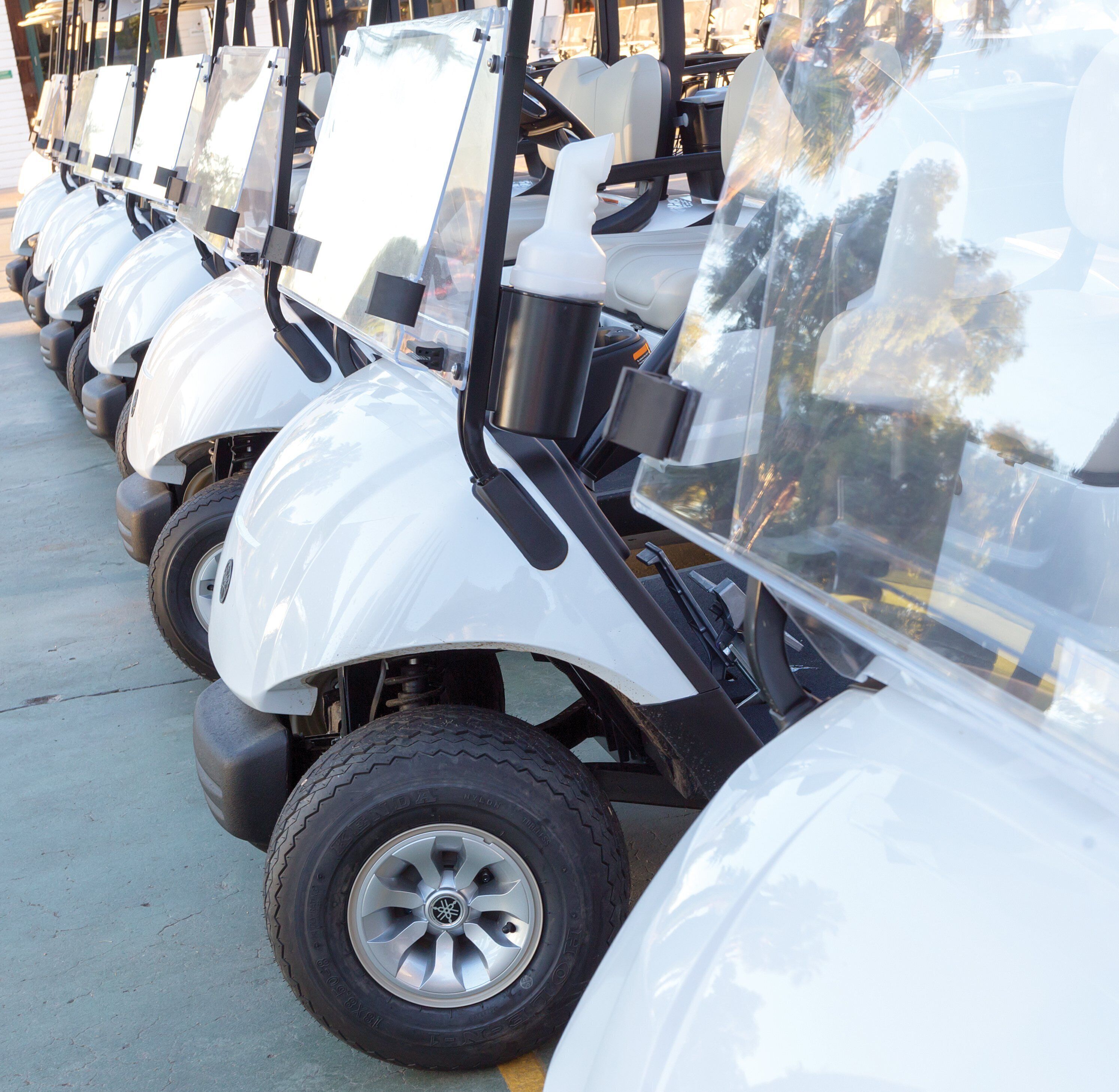 Una fila de carritos de golf blancos estacionados sobre una superficie de concreto.