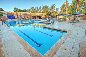 A swimming pool with clear blue water, surrounded by lounge chairs and umbrellas, with a view of trees and a building in the background. - Orange Tree Resort (Scottsdale)