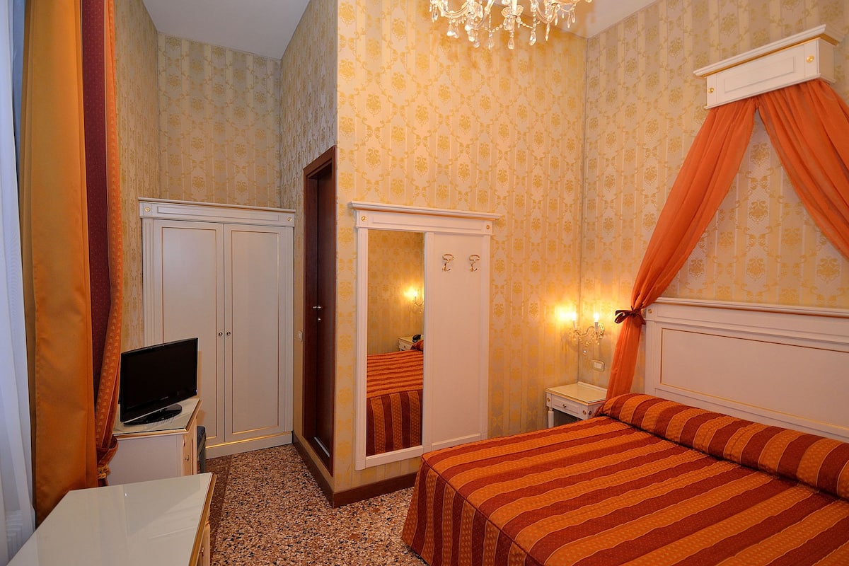 A bedroom with a bed, a television on a small table, a wardrobe, and a mirror.