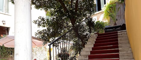 A staircase with red carpeted steps and a metal railing, leading to an outdoor area with tables and chairs.