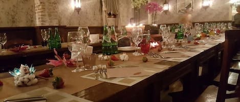 Una larga mesa de comedor dispuesta con múltiples copas de vino, botellas y cubiertos, lo que sugiere un ambiente de cena formal.
