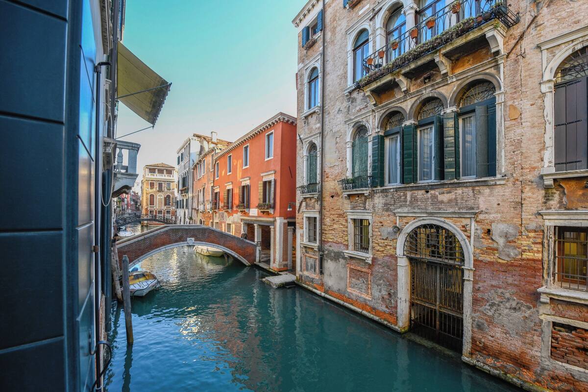 A narrow canal with buildings on either side, a bridge, and a boat.