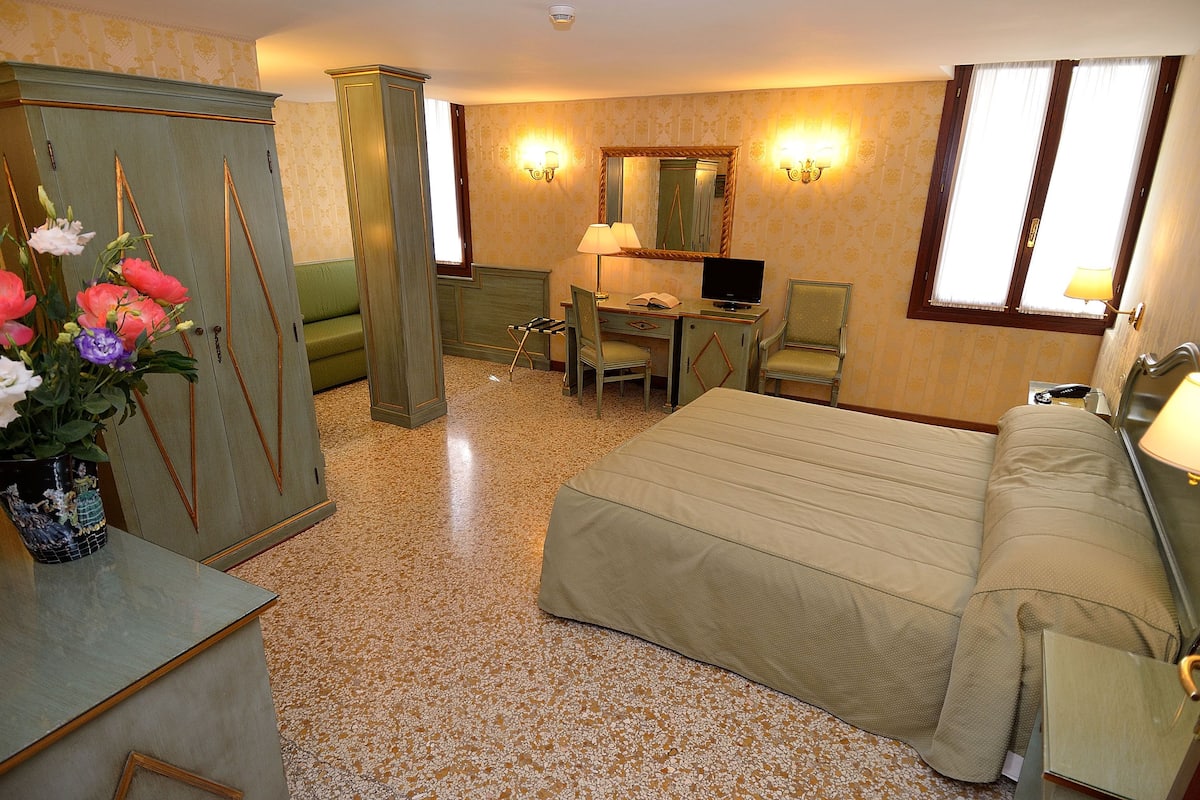 A hotel room with a bed, desk, chair, television, and a wardrobe.