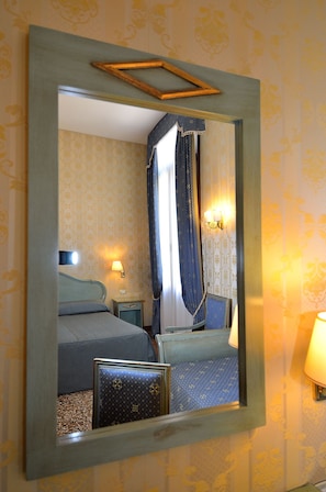A hotel room with a bed, bedside tables, a lamp, and a mirror.