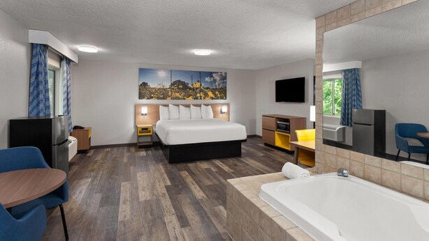 Une chambre d’hôtel moderne dotée d’un grand lit, d’un coin salon avec une table et des chaises, d’une baignoire et d’un téléviseur à écran plat.