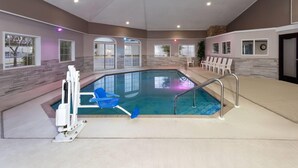 Une piscine intérieure avec un élément décoratif aquatique bleu, un escalier de piscine blanc et plusieurs chaises longues blanches.