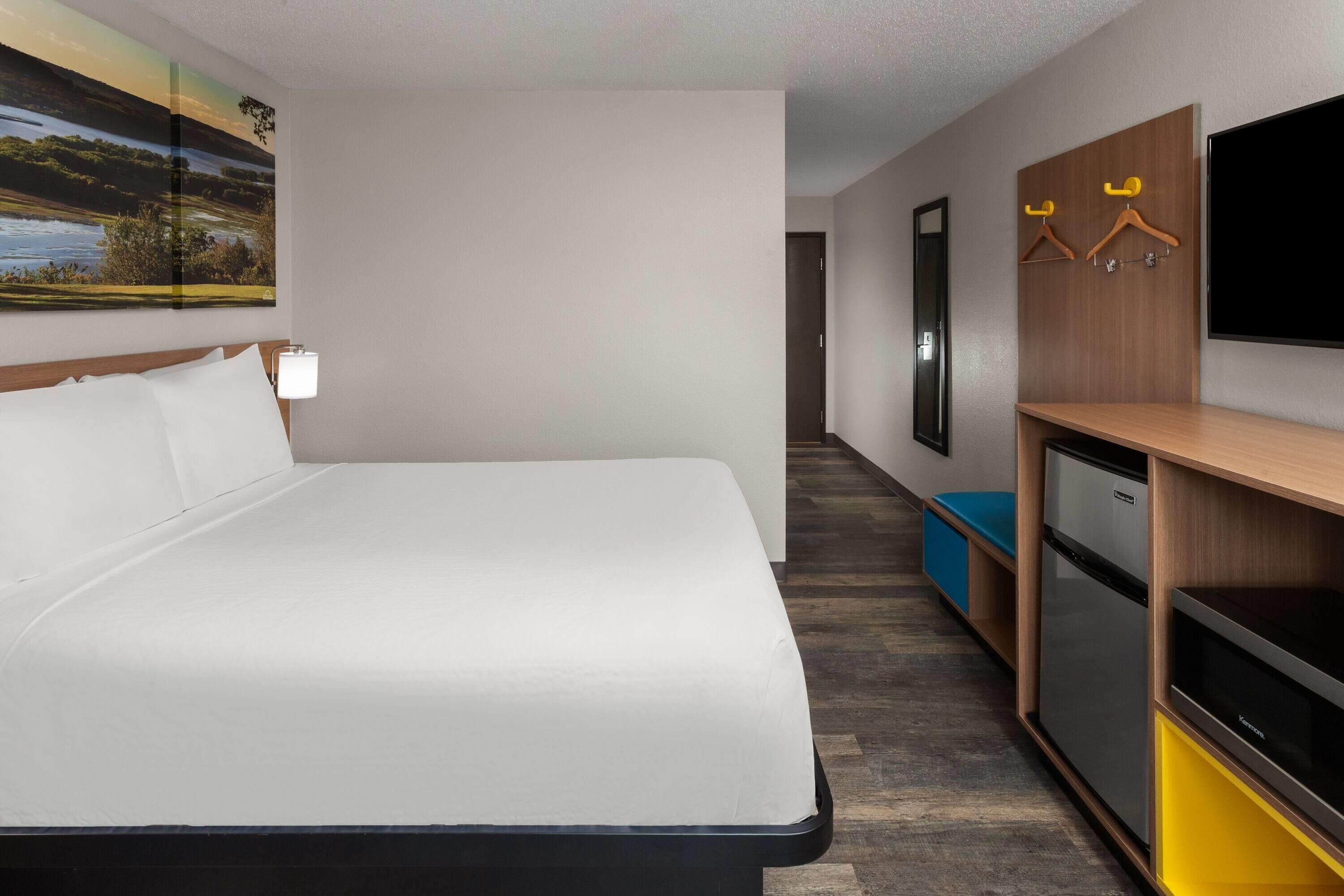 A hotel room with a bed, a TV, a desk with a computer, and a wall-mounted coat rack.