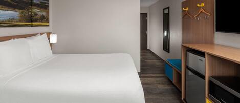 A hotel room with a bed, a TV, a desk with a computer, and a wall-mounted coat rack.