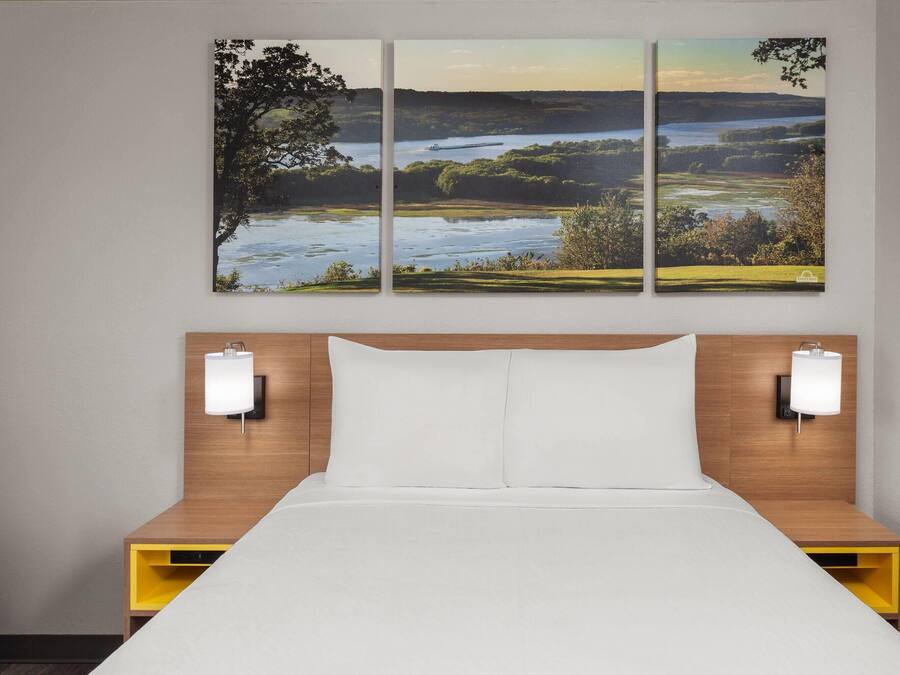A hotel room with a bed, two bedside tables, and a wall-mounted lamp.