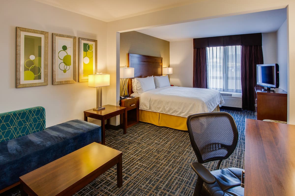 A hotel room with a bed, a desk, a chair, a sofa, and a television.