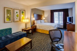 A hotel room with a bed, a desk, a chair, a sofa, and a television.