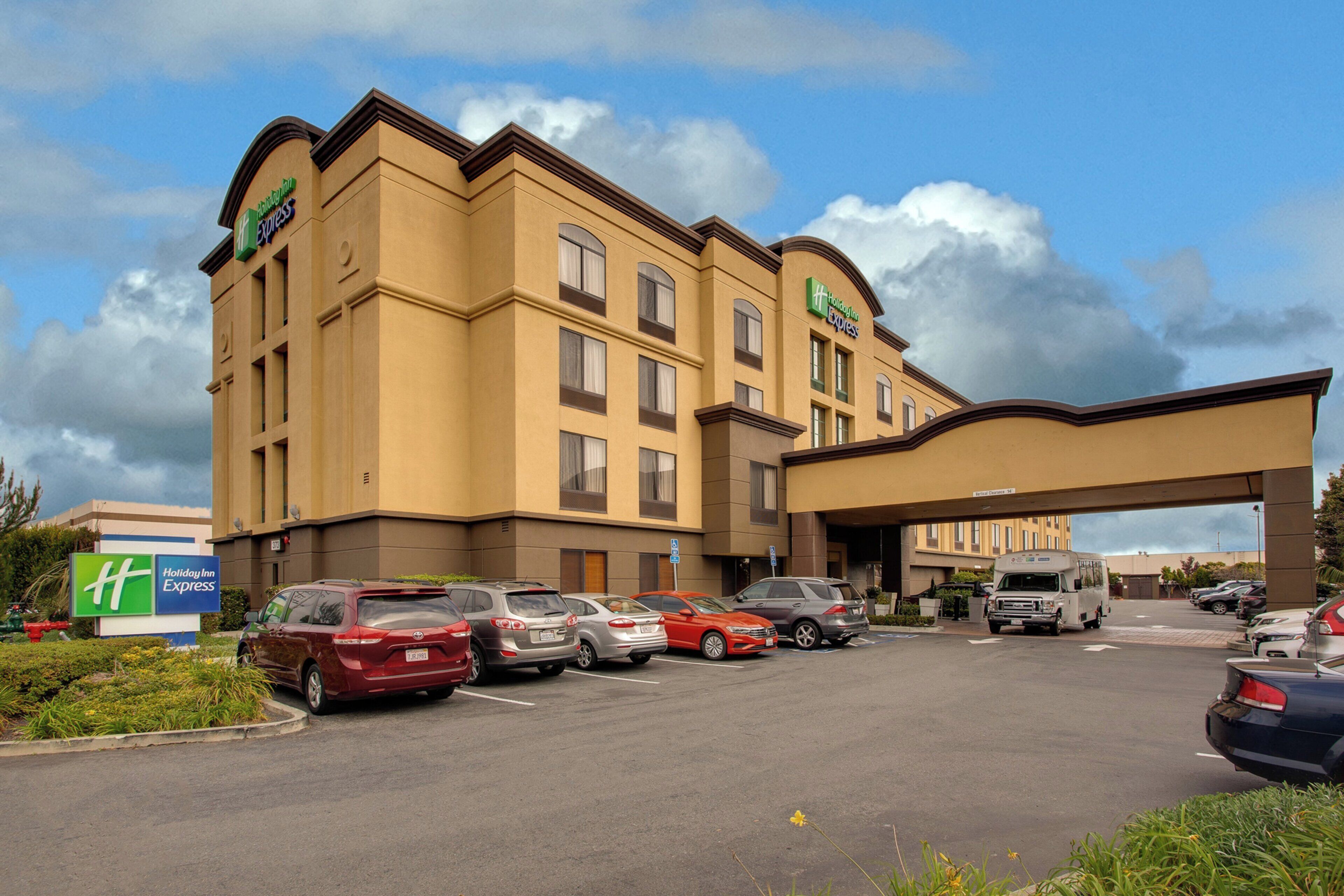 Un hôtel Holiday Inn Express avec un parking rempli de voitures, une passerelle couverte et un ciel dégagé.