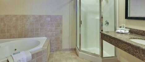A bathroom with a glass-enclosed shower, a white bathtub, and a granite countertop with a sink.