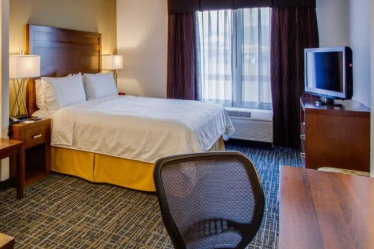 A hotel room with a bed, a desk, a chair, a television, and a window with curtains.
