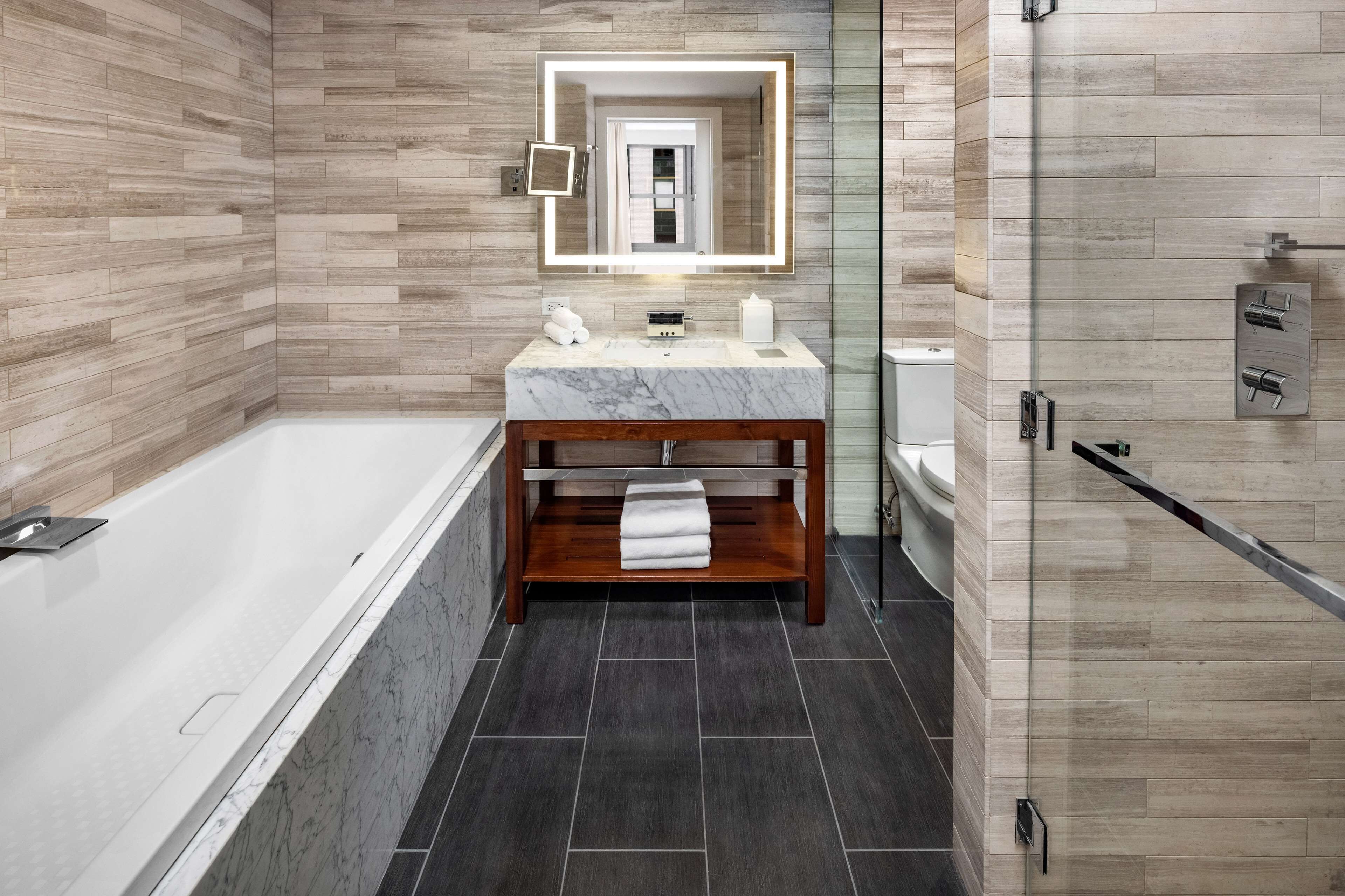 A modern bathroom with a marble vanity, a glass shower enclosure, and a wooden vanity with a towel.