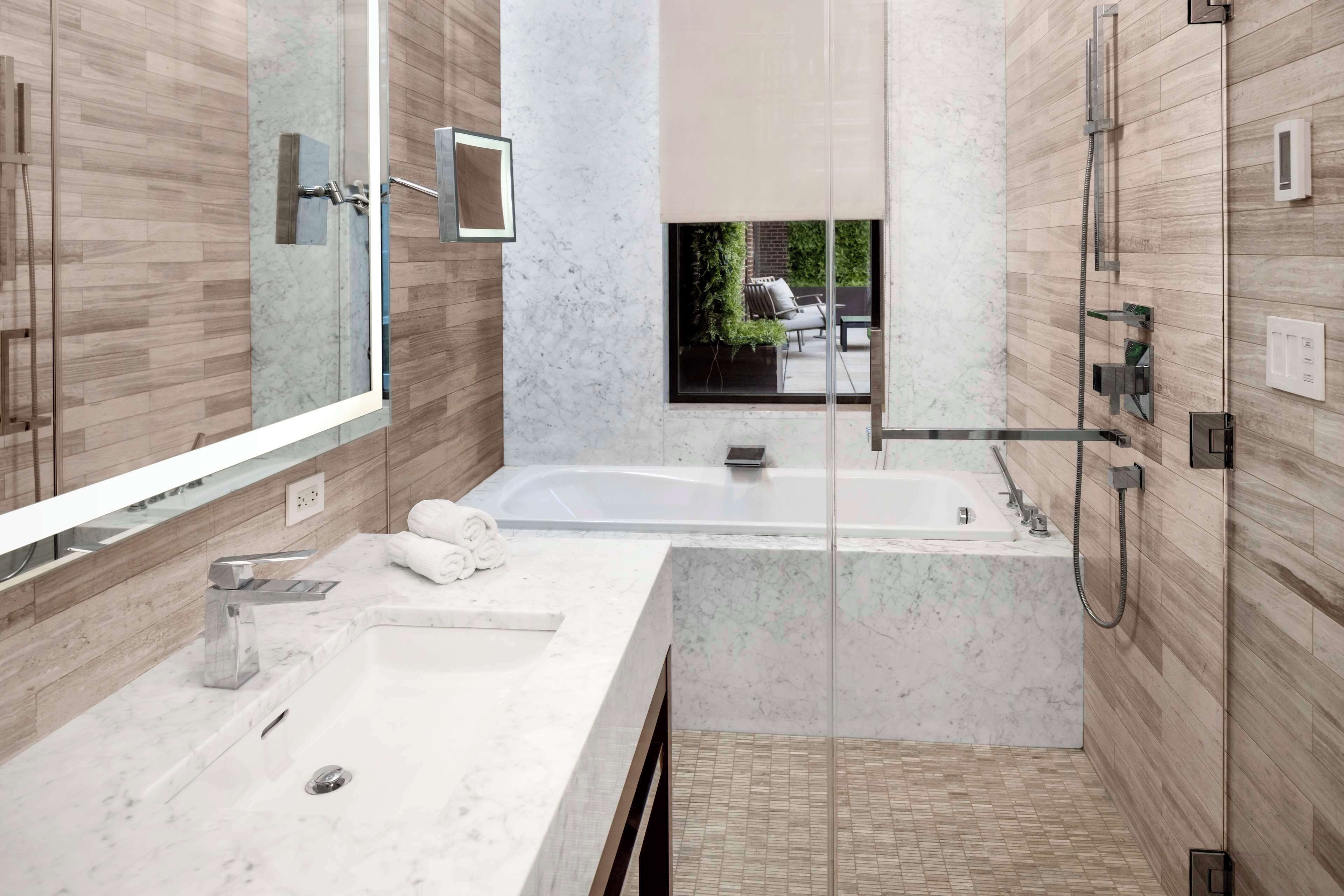 A modern bathroom with a large mirror, a bathtub, a shower area, and a sink.