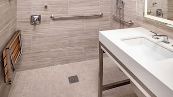 Un baño moderno con lavamanos blanco, ducha de mano, barra de apoyo y banco de madera.