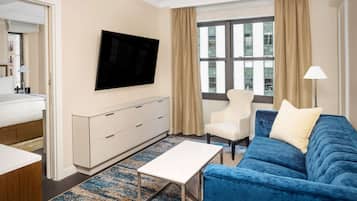 Une chambre d’hôtel avec un lit, un téléviseur fixé au mur, un canapé bleu, un fauteuil blanc et une petite table.